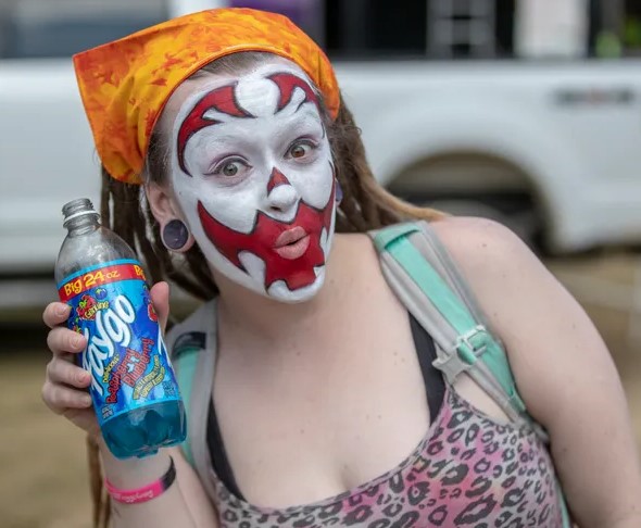 A woman in Juggalo makeup holding a 20oz Faygo.